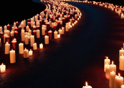 Attēlā redzams tumšs, izliektas formas ceļš, gar kura malām abās pusēs cieši rindās izvietoti daudzi desmiti iedegtu sveču. Sveces ir dažādos augstumos un krāsās – pārsvarā baltas, dažas sarkanbrūnas, un to liesmas gaiši apgaismo ceļu, radot siltu un piemiņas pilnu noskaņu. Ceļš un apkārtne ir iegrimuši tumsā, bet sveču gaismas vienmērīgi izgaismo gan pašu segumu, gan apkārtējo vidi. Attēla augšējā kreisajā stūrī redzams Rīgas starptautiskās autoostas logotips. Kopumā aina atstāj mierpilnu, cieņas un pārdomu pilnu iespaidu, līdzīgi kā piemiņas brīdī vai svinīgā vakara ceremonijā.