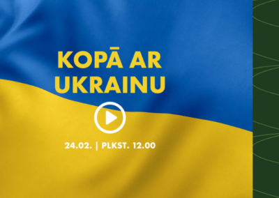 Attēlā redzams plakāts uz tumši zaļa, stilizēta fona. Centrā ir Ukrainas karogs ar zilo augšdaļu un dzelteno apakšdaļu. Uz karoga izvietots uzraksts “KOPĀ AR UKRAINU”, zem kura redzama balta atskaņošanas poga (trijstūra simbols aplī). Zem tās norādīts datums “24.02. | PLKST. 12.00”. Labajā apakšējā stūrī atrodas Rīgas starptautiskās autoostas logotips zaļā krāsā.