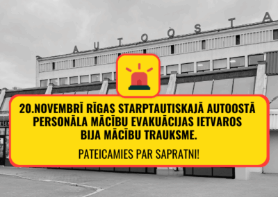 Rīgas starptautiskās autoostas ēkas fasāde melnbaltā tonī ar uzrakstu ‘AUTOOSTA’ augšpusē. Priekšplānā dzeltena informatīva zīme ar sarkanu apmali un sirēnas ikonu, kurā rakstīts: ‘20. novembrī Rīgas starptautiskajā autoostā personāla mācību evakuācijas ietvaros bija mācību trauksme. Pateicamies par sapratni!’ Attēla kreisajā augšējā stūrī autoostas logotips